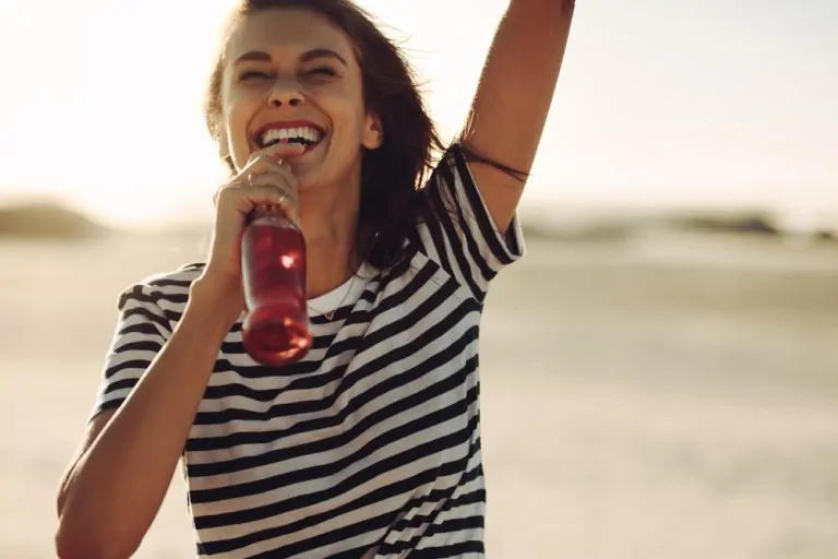 Cheerful,Young,Woman,Standing,Outdoors,And,Drinking,Cola,From,Glass